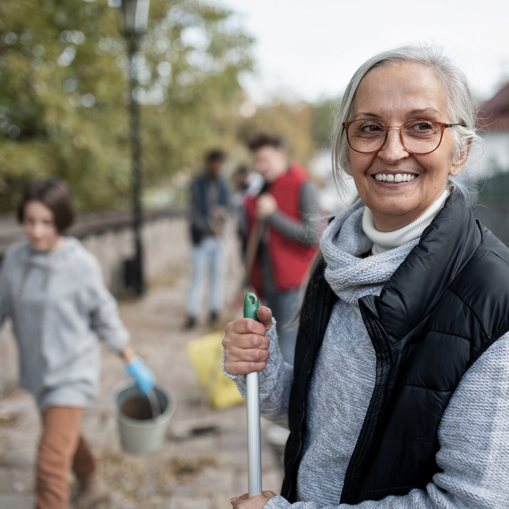 Happy senior woman volunteer with team cleaning up street, community service concept